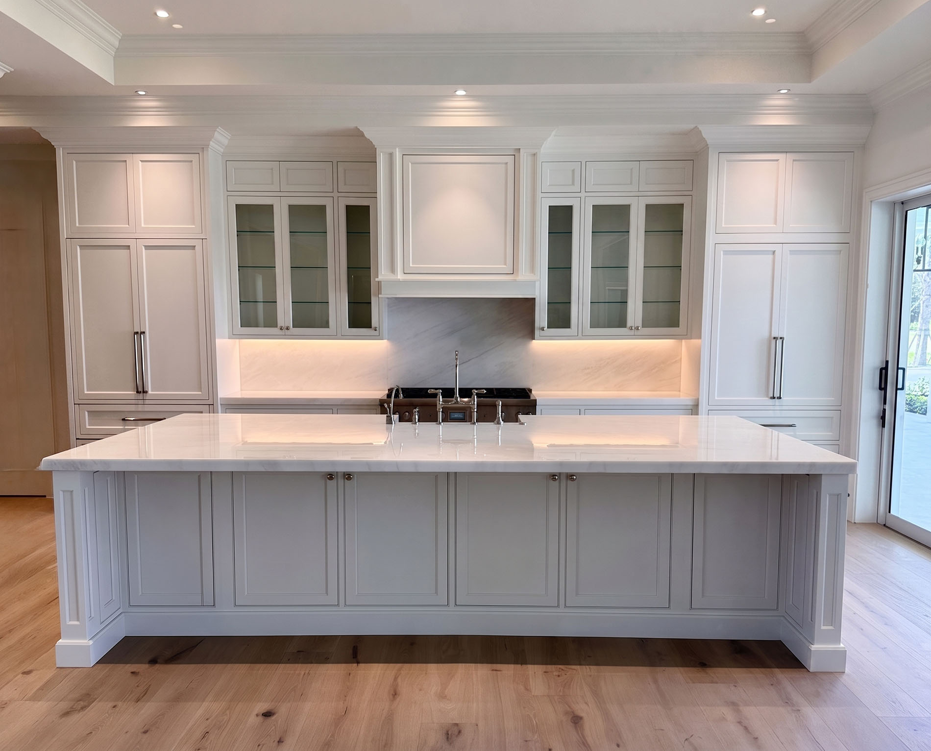 Symmetrical white kitchen with a long marble island, glass-front uppers, and professional range